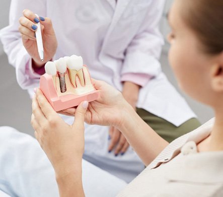 Dentist pointing to a dental implant model that patient is holding