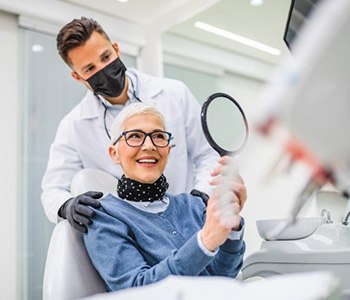 Woman admiring her smile in small mirror with dentist standing behind her 