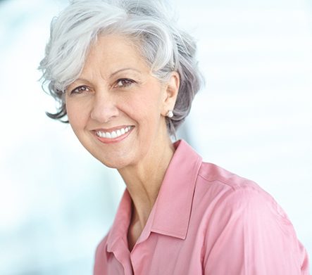 Hands holding transparent pink model jaw with 2 dental implants and a dental bridge