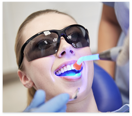 Dental patient having ultraviolet light shone on her tooth by cosmetic dentist