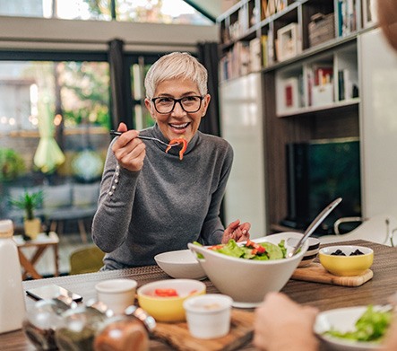 Woman with black glasses smiling while eating with friend