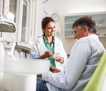 Smiling dentist showing patient model of teeth