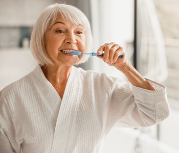 woman brushing her teeth in bathroom mirror