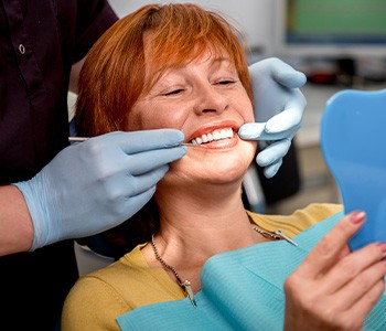 woman smiling while holding dental mirror