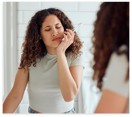 Woman with toothbrush holding her cheek in pain before T M J treatment