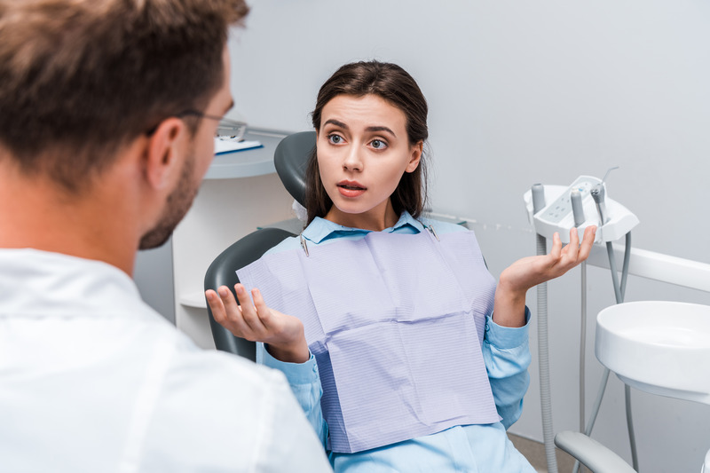 Patient with questionable oral health shrugging at dentist